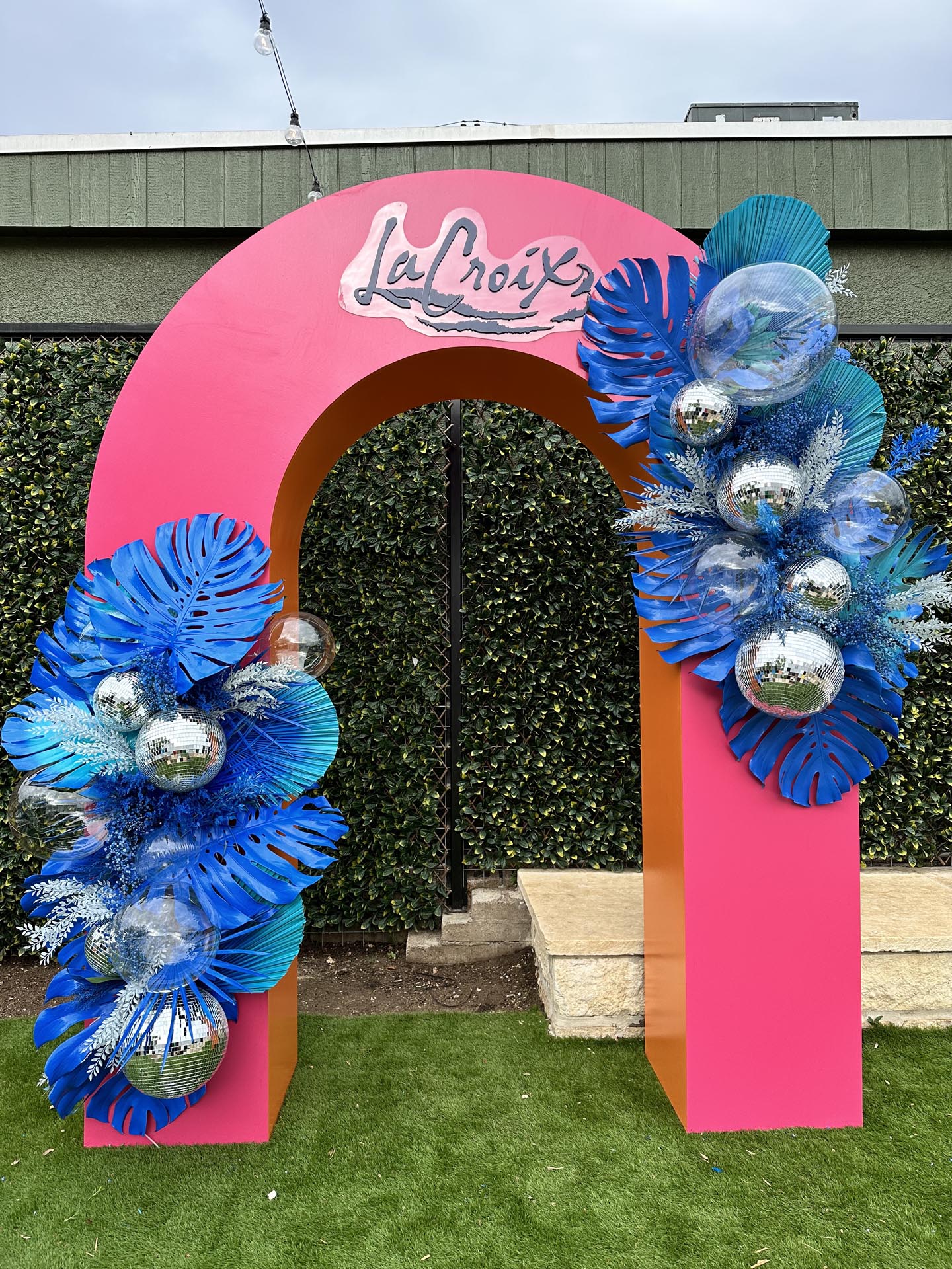 A pink and orange arch for La Croix at SXSW 2023 featuring blue floral arrangements and disco balls