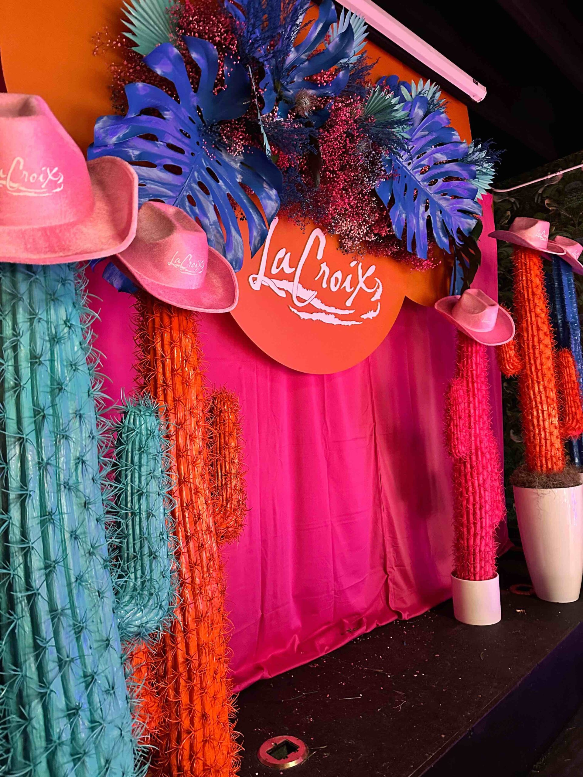 Colorful backdrop with neon cacti decor and blue and purple floral arrangements for LaCroix House at SXSW 2023